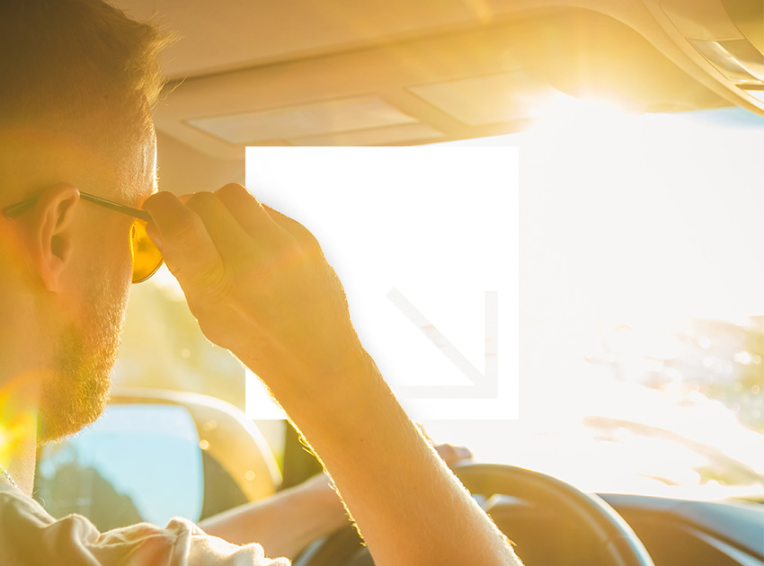 Driver adjusting sunglasses while driving in bright, hot sunlight.