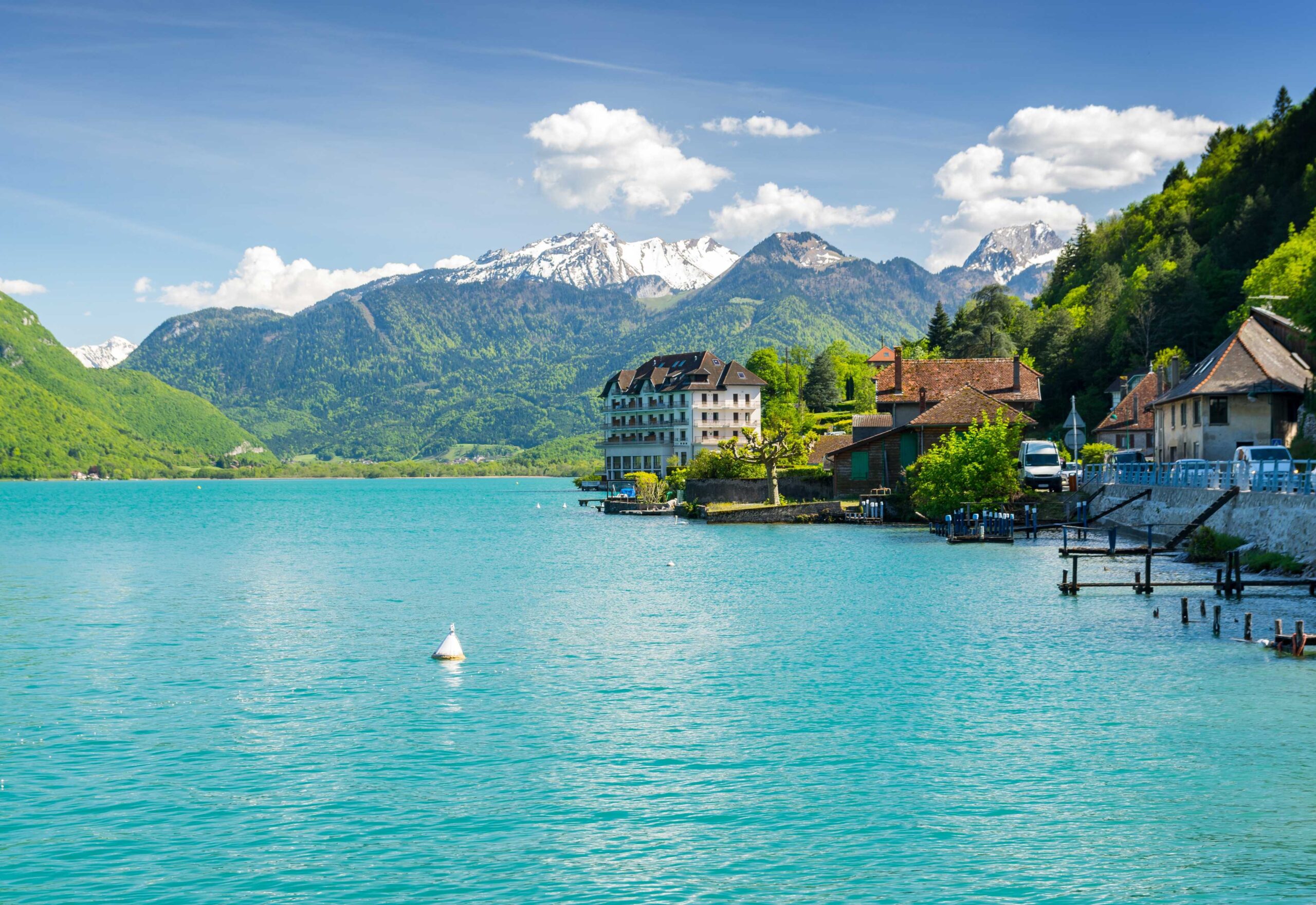 View of the snow-capped French Alps on the turquoise water of Lake Annecy.