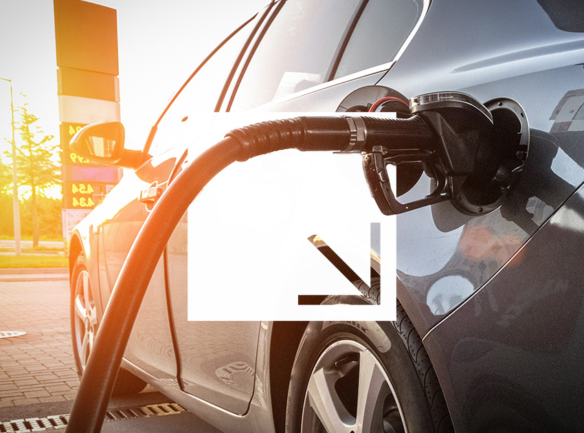 Fuel nozzle inserted into a car at a petrol station during sunset.