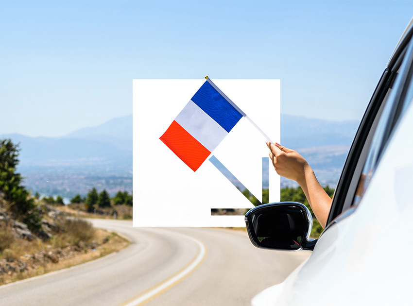French flag held out of a car window while driving on a rural road, highlighting travel safety and car hire excess insurance.