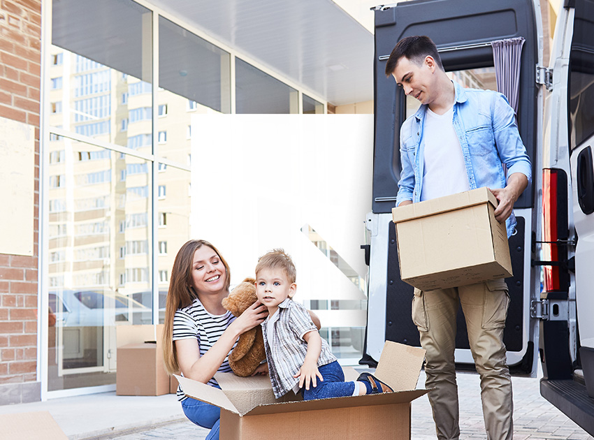 Young family unpacking boxes outside their new home, a reminder that car hire excess insurance prevents surprise fees when renting vehicles for big moves.