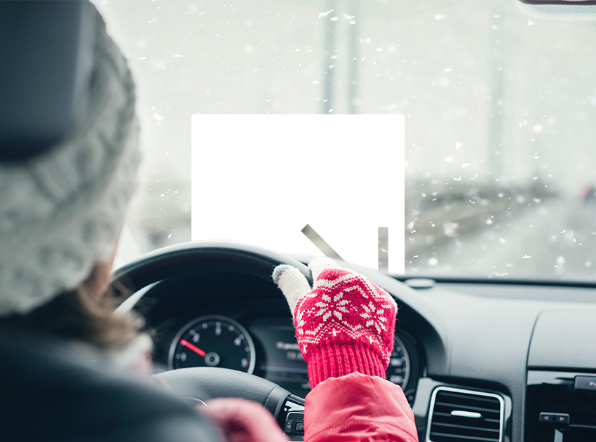 Woman holding the steering wheel driving in the snow with red gloves on.